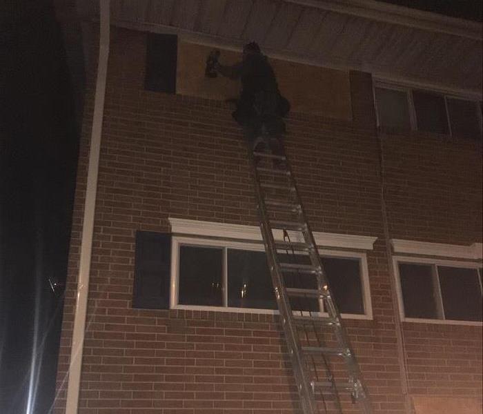 SERVPRO employee on a ladder boarding up a window