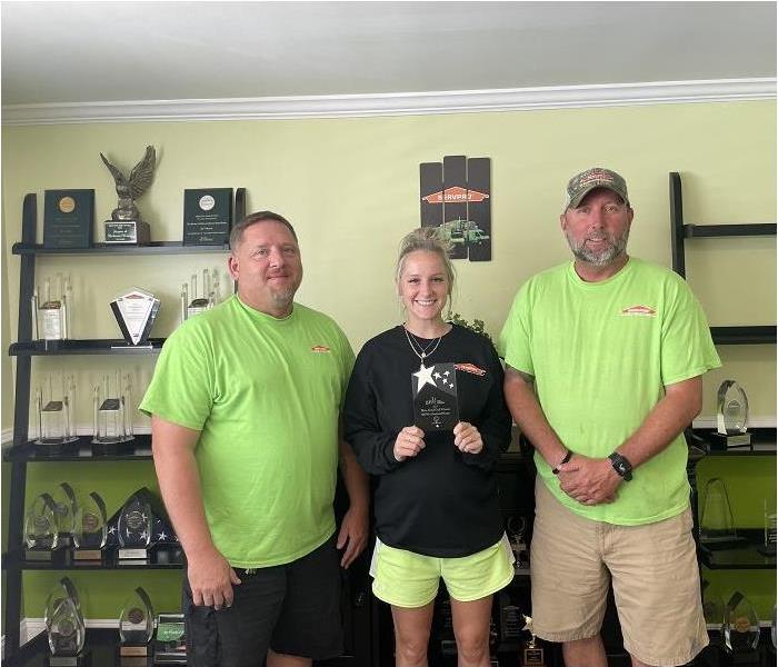 3 SERVPRO team members posing with lady in middle holding plaque